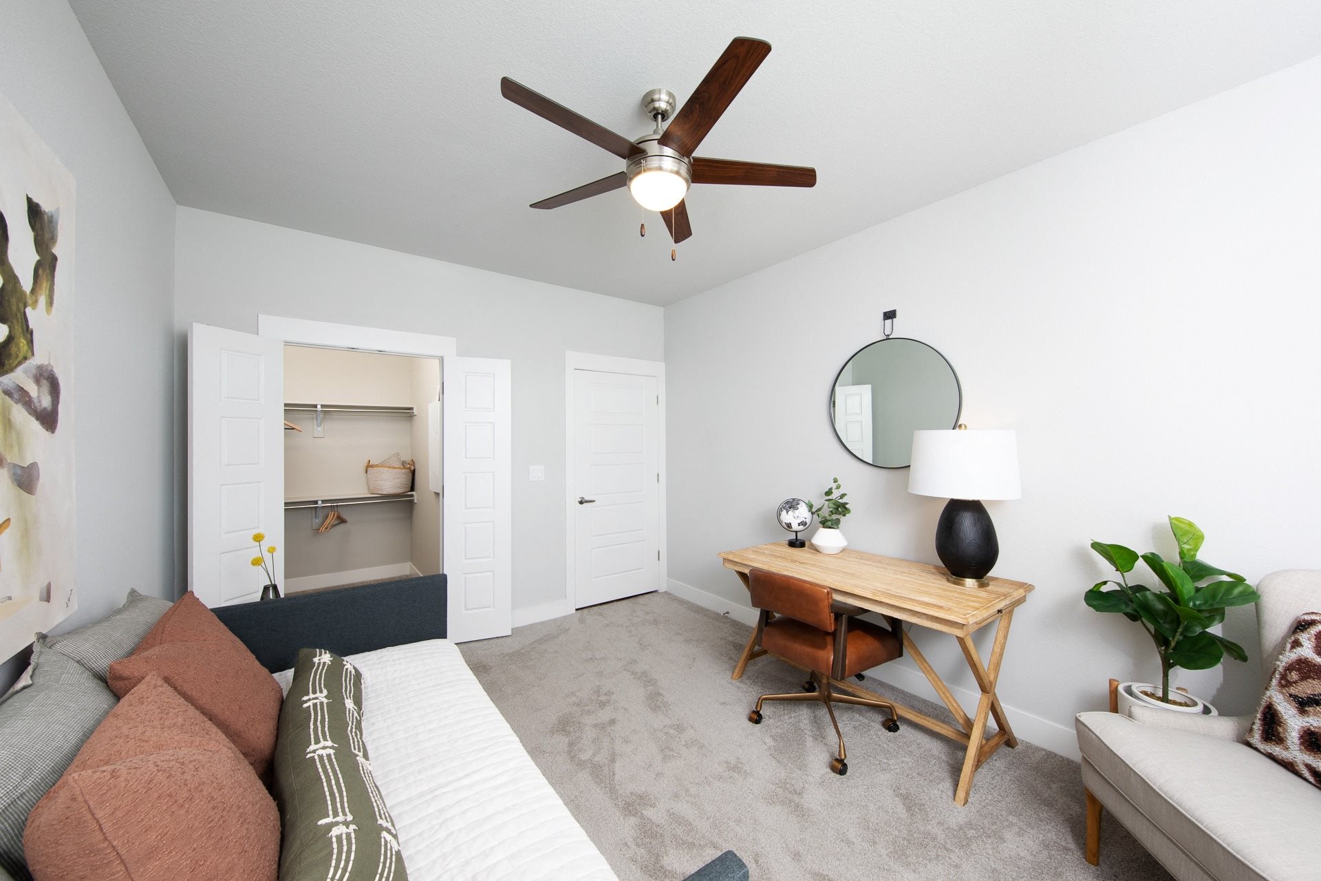 a bedroom with a daybed, desk, and ceiling fan at a senior apartment community